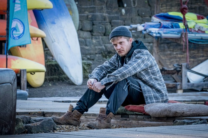 Tom Glynn-Carney as Malachy in The Jetty sitting in a chequered shirt and woolly hat