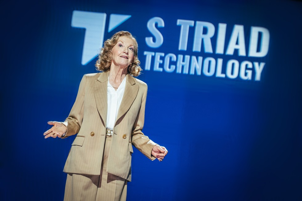 Susan Twist as Susan Triad in Doctor Who: The Legend Of Ruby Sunday. She is presenting in front of a backdrop saying "S Triad Technology"