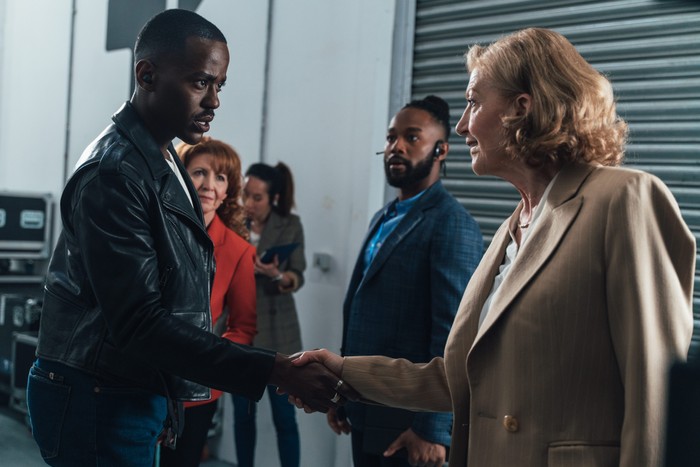 Ncuti Gatwa as The Doctor, Bonnie Langford as Mel and Susan Twist as Susan Triad in Doctor Who. The Doctor is shaking Susan's hand.