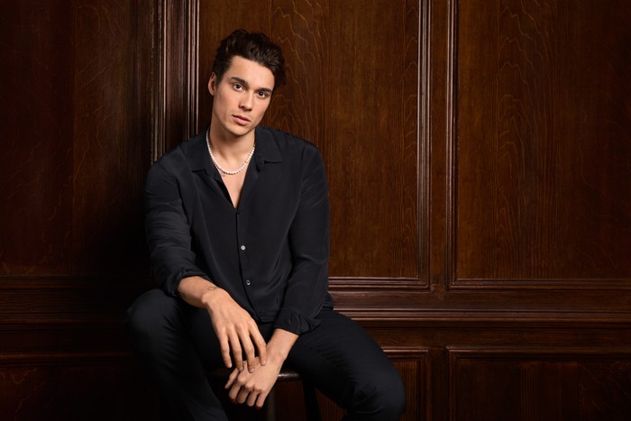 Miles Nazaire pictured for Made in Chelsea. He is wearing a black shirt and black trousers.