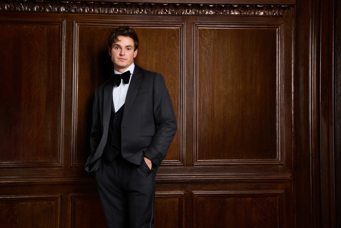 Sam Prince pictured for Made in Chelsea. He is wearing a full tuxedo and has his hand in his pocket and is looking ahead.