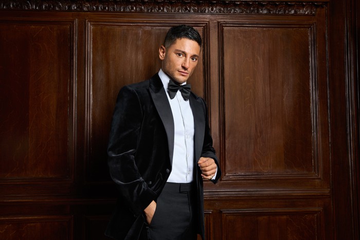 Reza wearing a tuxedo, being pictured for Made in Chelsea season 27. He has one hand in his pocket and the other above.