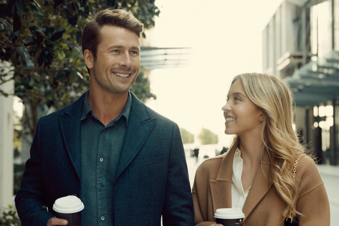 Anyone But You Glen Powell and Sydney Sweeney walking together with coffee cups smiling