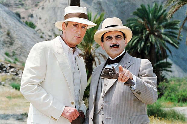 David Suchet as Hercule Poirot standing next to a man in a white linen suit looking into camera