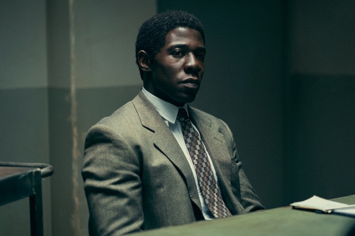 McKinley Belcher III as Ledroit sitting at a table in a police station interrogation room with a stern look on his face.