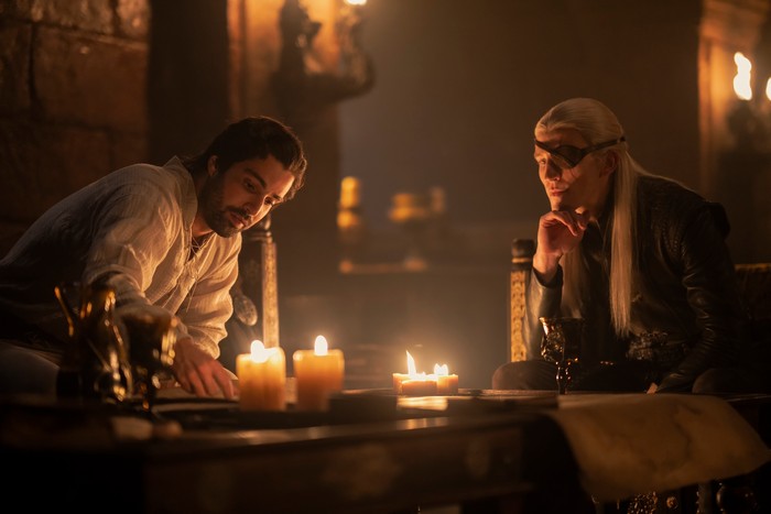 Fabien Frankel as Ser Criston Cole sits by candlelight with Ewan Mitchell as Prince Aemond Targaryen in House of the Dragon season 2.