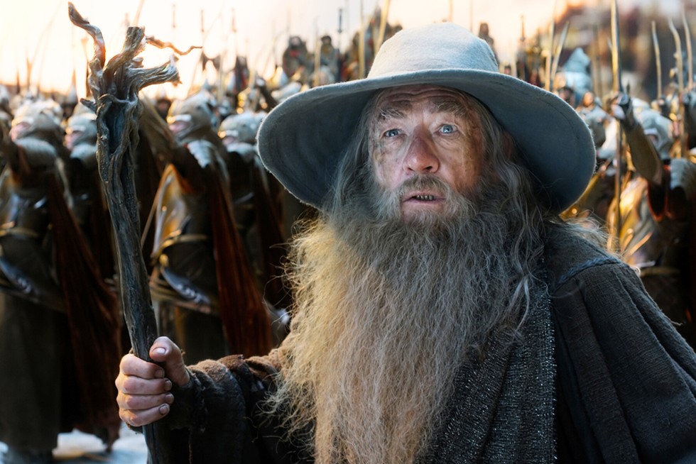 Sir Ian McKellen as Gandalf in a robe and wizard's hat holding a staff. An army of soldiers are behind him