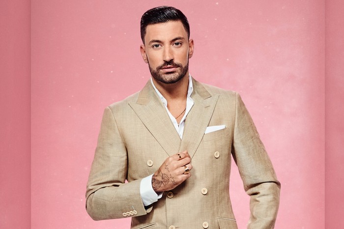 Giovanni Pernice wears a light-coloured suit and stands before a pink background