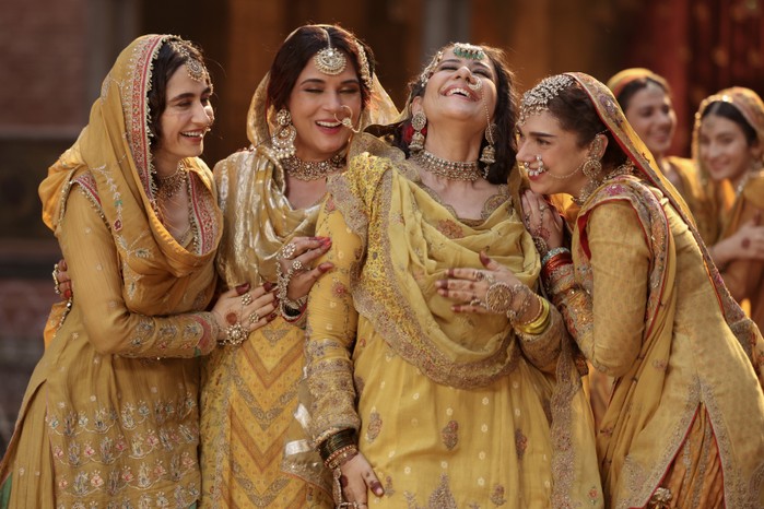 Sanjeeda Sheikh as Waheeda, Richa Chadha as Lajjo, Manisha Koirala as Mallikajaan, Aditi Rao Hydari as Bibbo all wearing matching yellow sarees and holding each other, laughing in Heeramandi: The Diamond Bazaar.