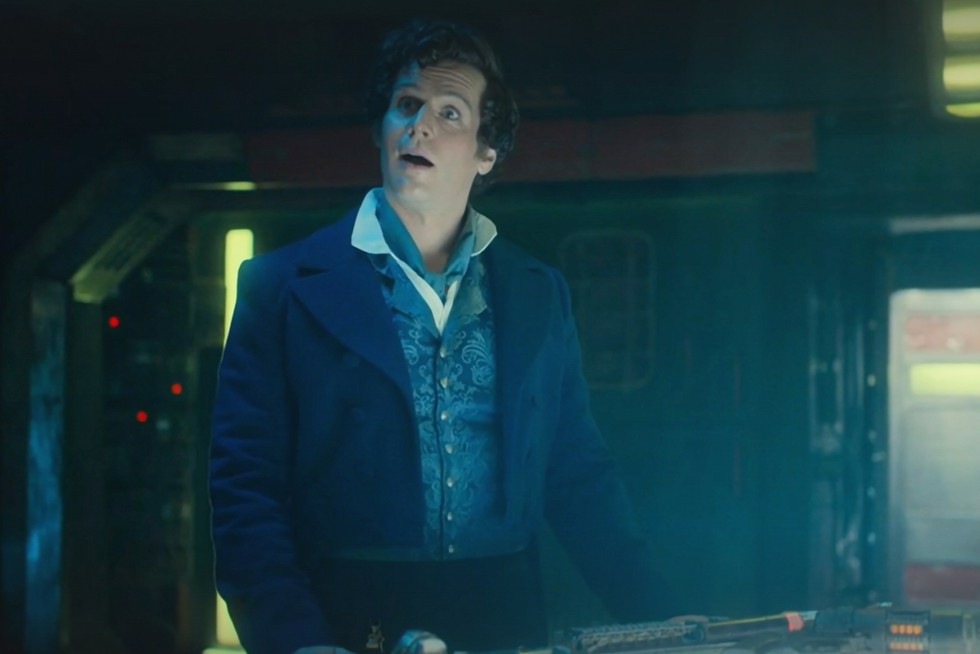 Jonathan Groff as Rogue in Regency attire standing by the TARDIS control panel