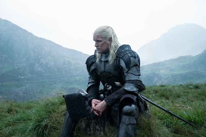 Matt Smith perched on grass in armour with long platinum hair as Prince Daemon Targaryen in House of the Dragon season 2.