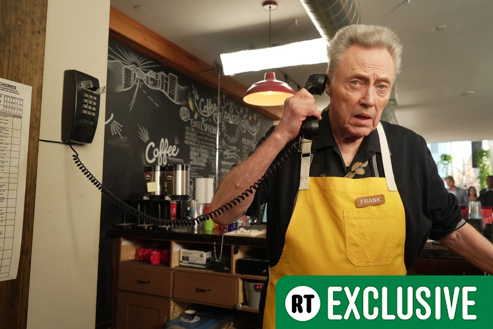 Frank (Christopher Walken) wearing a yellow apron while working in a cafe, holding a wired landline phone to his ear