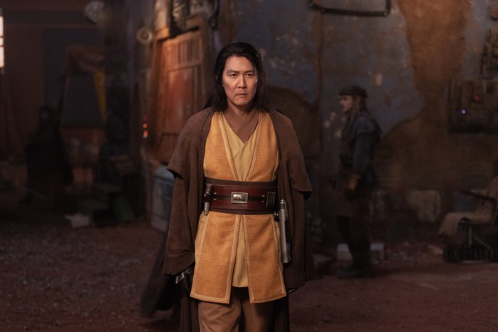 Lee Jung-jae as Master Sol in The Acolyte in a brown and yellow robe with lightsaber on his belt