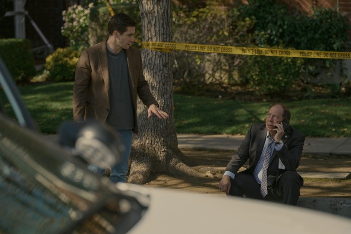 Jake Gyllenhaal and Bill Camp in Presumed Innocent. There is police tape behind them and Camp is sat on the floor