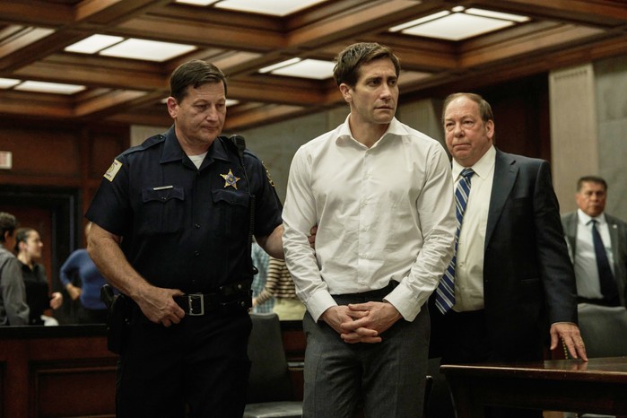 Jake Gyllenhaal and Bill Camp in Presumed Innocent standing together in a courtroom next to a police officer