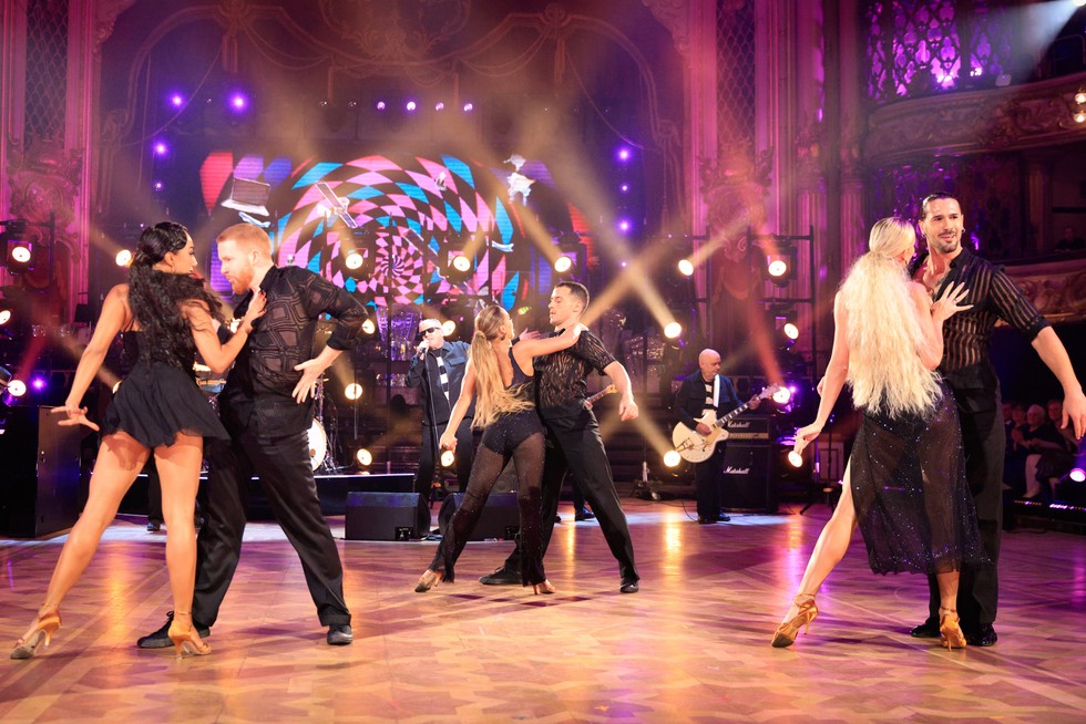 Strictly Come Dancing professionals dancing in three pairs of two on the ballroom floor, with Madness performing in the background.