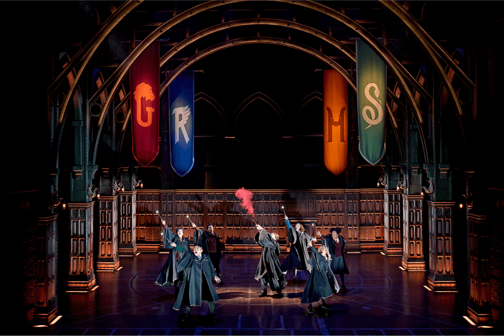 Wizarding student pointing their wands under the banners of the Hogwarts houses